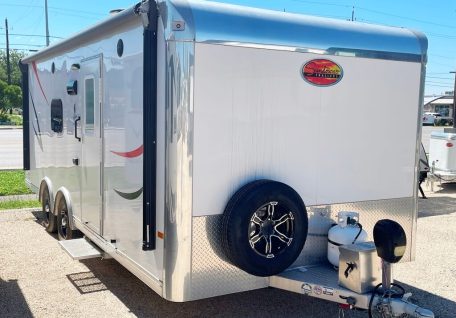 A shiny aluminum trailer with a sleek design, featuring a spare tire, propane tank, and subtle colorful accents.