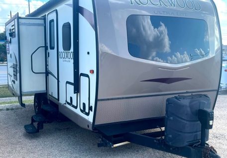 A Rockwood Ultra Lite travel trailer parked outdoors, featuring a slide-out section and reflecting clouds in its windows.