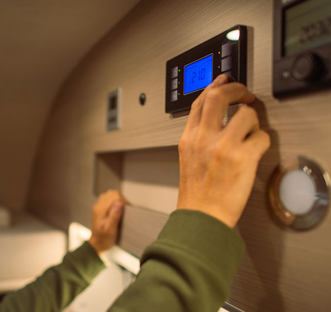 A hand adjusts a digital thermostat displaying 210 on a sleek wooden panel inside a modern RV or camper.